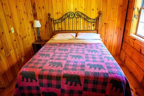 A wooden-paneled room with a bed, a nightstand, a lamp, and a window.