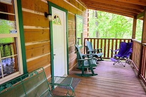 A wooden cabin with a porch, green metal chairs, and a blue folding chair.