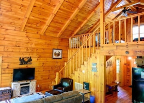 A wooden cabin interior with a staircase, a fireplace, a television, and a couch.