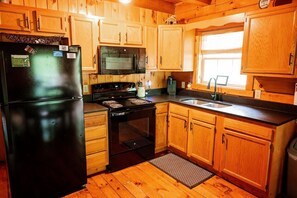 Uma cozinha rústica em estilo cabana, com geladeira, micro-ondas, fogão e pia.