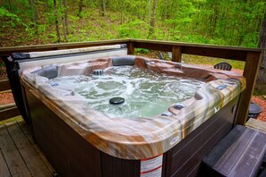 A hot tub on a wooden deck surrounded by a forest.
