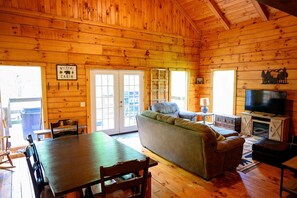 A cabin interior with a dining table, sofa, television, and a sign reading 'Welcome to the Cabin.'