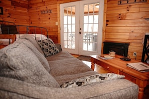 A cozy log cabin room with a sofa, a small table, a fireplace, and a door leading outside.