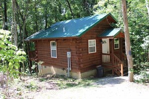 A wooden cabin with a green roof, a porch, and a small front door.