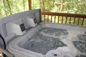 A hot tub with a wooden deck and a view of a forest.