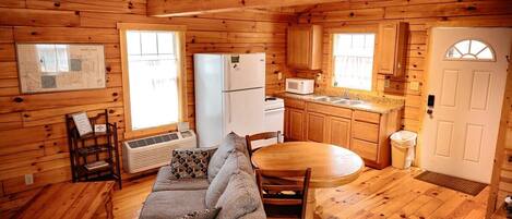 A wooden cabin interior with a sofa, dining table, kitchen area, and a map on the wall.