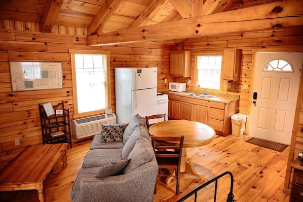 A wooden cabin interior with a sofa, dining table, kitchen area, and a map on the wall.