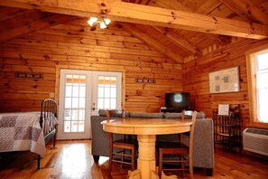 Interior de una cabaña de madera con una mesa de comedor, sillas, un sofá, un televisor y un mapa en la pared.