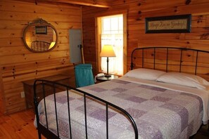 Una habitación tipo cabaña de madera con cama, un espejo redondo, una lámpara y un letrero en la pared.