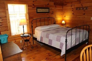 Una habitación de cabaña de madera con una cama, dos lámparas de noche, una mesita y una ventana con cortinas.