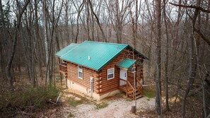 Una cabaña de madera con techo verde, rodeada de árboles.