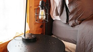 Une pièce chaleureuse avec un lit, une table ronde surmontée d’une lampe et des murs en bois.