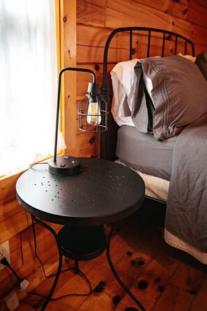 A cozy room with a bed, a round table with a lamp, and wooden walls.