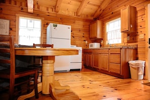 A wooden cabin interior with a kitchen area featuring a refrigerator, microwave, wooden cabinets, and a dining table with chairs.