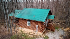 A log cabin with a green roof, a front porch, and a small deck.