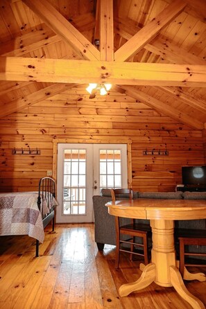 A log cabin interior with a bed, sofa, dining table, and a television.