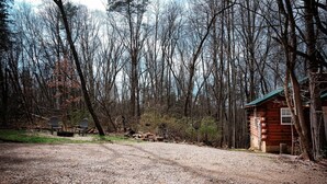 Un chalet rustique, accessible par un sentier de terre, et entouré d’une forêt dense.