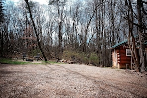 A rustic cabin with a dirt path leading to it, surrounded by a dense forest.