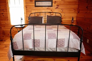A wooden-paneled room with a metal-framed bed, a framed quote on the wall, and a window with blinds.