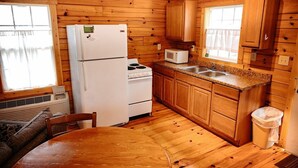 Une cuisine rustique, située dans une cabane en bois, équipée d’un réfrigérateur, d’une cuisinière, d’un four à micro-ondes, d’un évier et de meubles de rangement en bois.