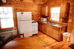 A wooden cabin kitchen with a refrigerator, stove, microwave, sink, and wooden cabinets.