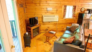 A wooden interior with a sofa, television, fireplace, and a clock on the wall. - Lazy Lane Cabins - Wren's Nest (Logan)