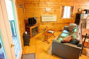 A wooden interior with a sofa, television, fireplace, and a clock on the wall.