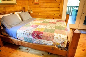 A wooden bed with a quilt, a nightstand, and a wooden headboard in a room with wooden walls and floors.