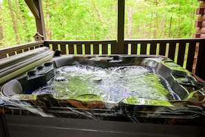 Un jacuzzi con caída de agua, rodeado por una terraza de madera y un fondo de bosque.