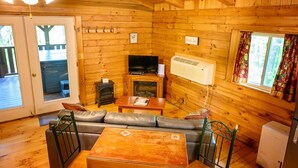 A log cabin interior with a sofa, television, fireplace, and wooden walls. - Lazy Lane Cabins - Wren's Nest (Logan)