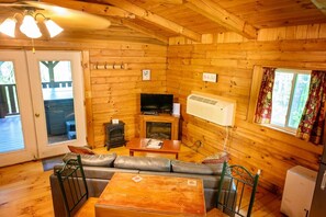 A log cabin interior with a sofa, television, fireplace, and wooden walls.
