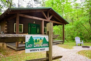 A cabin with a porch, a green door, and a sign reading 'Lazy Lane Cabins Wren's Nest.'