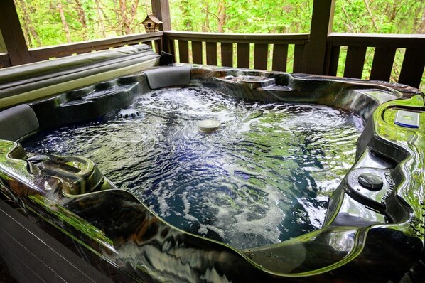 A hot tub with a wooden deck and a view of greenery.