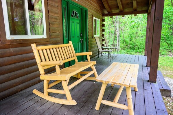A wooden rocking chair and table on a porch with a green door and windows.