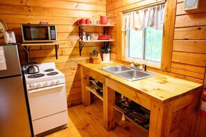 A compact kitchen with a microwave, stove, sink, and wooden cabinets.