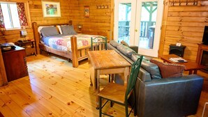 A wooden cabin interior with a bed, sofa, dining table, and a fireplace. - Lazy Lane Cabins - Wren's Nest (Logan)