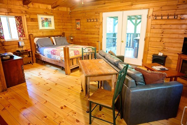 A wooden cabin interior with a bed, sofa, dining table, and a fireplace.