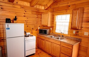 A compact kitchen with wooden walls, a refrigerator, stove, microwave, and two sinks.