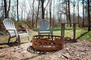 A campsite with two Adirondack chairs, a metal fire pit, and a picnic table.