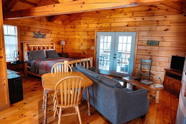 A cozy cabin with a bed, a dining table, a sofa, and a TV.