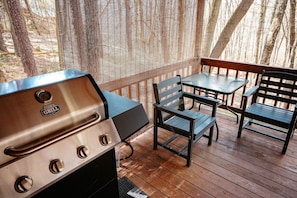 An outdoor deck with a grill, two wooden chairs, and a table.