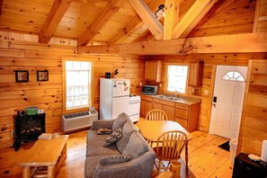 Interior de uma cabana com sala de estar, cozinha compacta e uma porta.