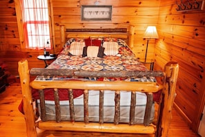 A wooden cabin room with a bed, a lamp, and a framed picture on the wall. - Lazy Lane Cabins - Buckeye (Logan)