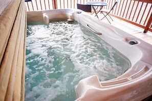 A hot tub with a handle, surrounded by a wooden deck and outdoor furniture. - Lazy Lane Cabins - Buckeye (Logan)