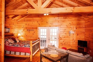 A log cabin interior with a bed, a sofa, a glass table, and a television.