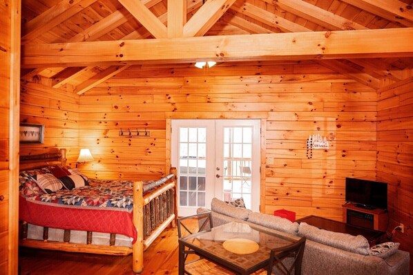 A log cabin interior with a bed, a sofa, a glass table, and a television.