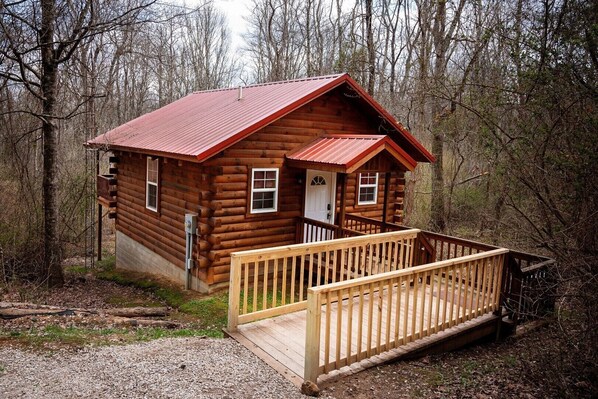 A log cabin with a wooden deck and a metal roof.