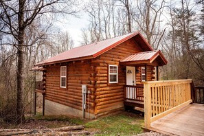 A wooden cabin with a porch, a small deck, and a door with a window.
