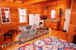 A log cabin with a kitchenette, a sofa, a quilt, and a wooden bench.