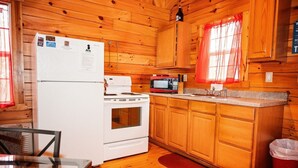 A wooden cabin kitchen with a refrigerator, stove, microwave, and wooden cabinets. - Lazy Lane Cabins - Buckeye (Logan)